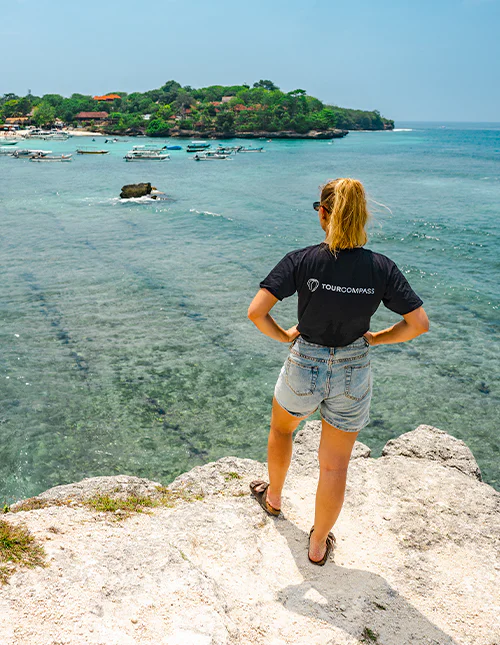 Vrouw in een TourCompass T-shirt geniet van het uitzicht op het turkooisblauwe water
