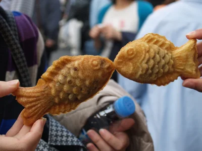 Twee mensen houden taiyaki's omhoog, zodat het lijkt alsof de visjes zoenen