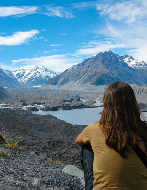 Persoon die uitkijkt over de met sneeuw bedekte bergen en het gletsjermeer in Aoraki/Mount Cook National Park, Nieuw-Zeeland