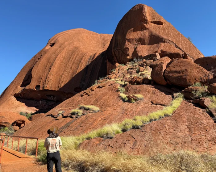 Uluru in Australië met een wandelaar aan de voet van de enorme rode rotsformatie