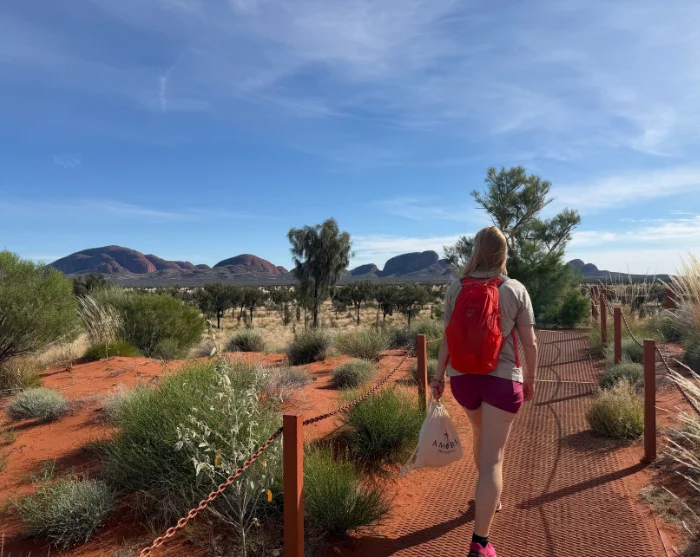 Vrouw met een rode rugzak op weg naar een uitzichtpunt bij Kata Tjuta in Australië, met de rode rotsen op de achtergrond