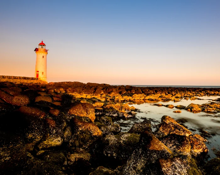 De vuurtoren van Port Fairy in Australië, een witte vuurtoren met een rood dak aan een rotsachtige kust in de avondzon
