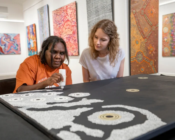 Kunstenaar schildert Aboriginalkunst in de Gallery of Central Australia in Australië, terwijl een vrouw toekijkt
