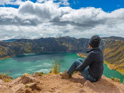 Een vrouw zit aan de rand van het Quilotoa-kratermeer in Ecuador.