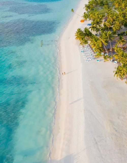 Wit zandstrand en turkooisblauwe zee met palmbomen, vanuit de lucht gezien