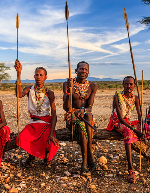 Een groep Maasai zit op de savanne, met speren in hun handen