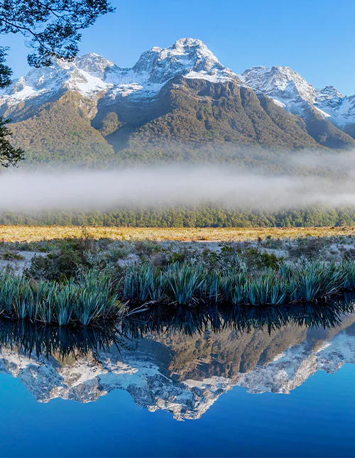 Mirror Lake, laaghangende mist en met sneeuw bedekte bergtoppen op een heldere winterdag in Milford Sound, Nieuw-Zeeland