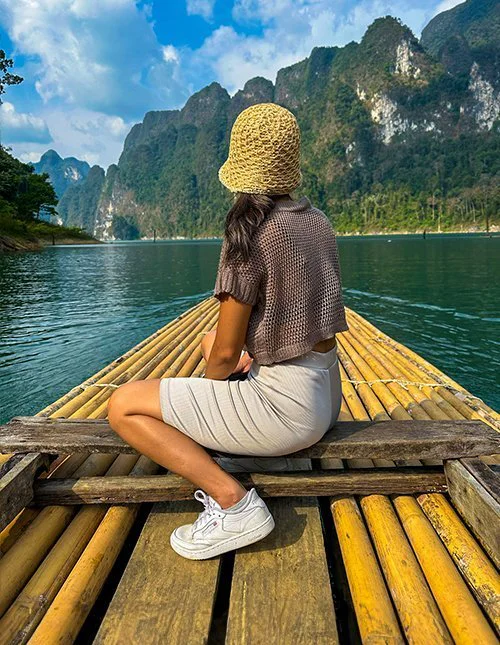 Een vrouw glijdt op een bamboevlot over een Thais meer, omringd door imposante kalksteenbergen.
