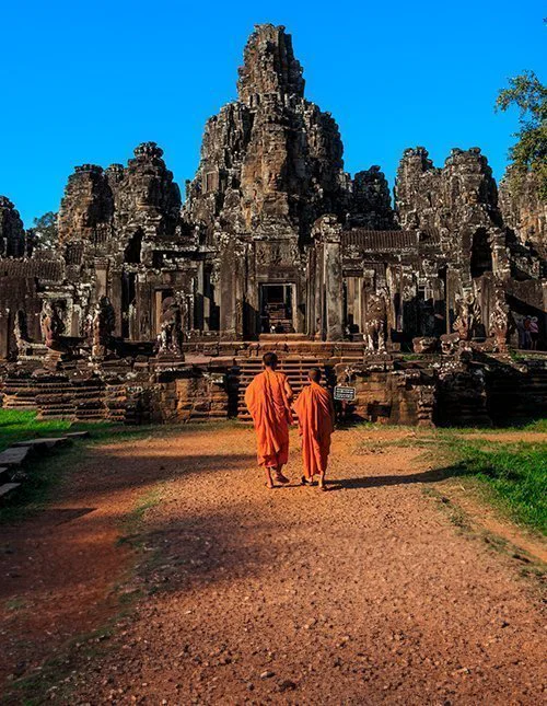 Monniken tussen de eeuwenoude stenen gezichten van de Bayon-tempel, Angkor, Cambodja