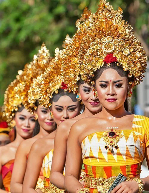Traditionele Balinese dansers in kleurrijke kostuums en met gouden hoofdtooien tijdens een processie.