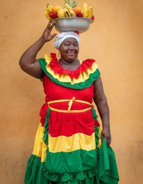Lachende Colombiaanse vrouw met een fruitschaal op haar hoofd