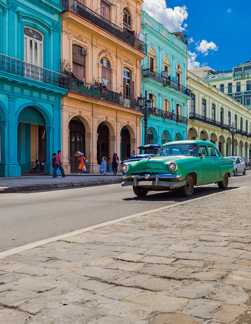 Kleurrijke koloniale gebouwen in Cuba en een klassieke groene auto in een zonnige stadsstraat.