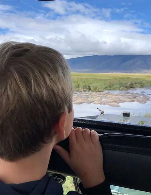 Een kind kijkt vanuit een safarivoertuig uit over een rivier en de savanne