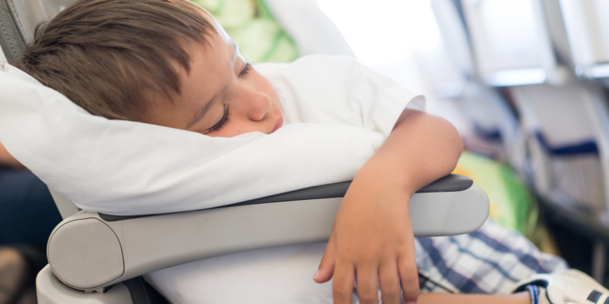 Jongen slaapt met een kussen in het vliegtuig