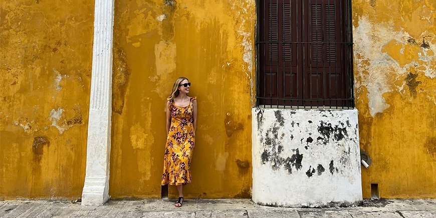 Vrouw in oranje jurk leunt tegen oranje muur in Izamal, Mexico.