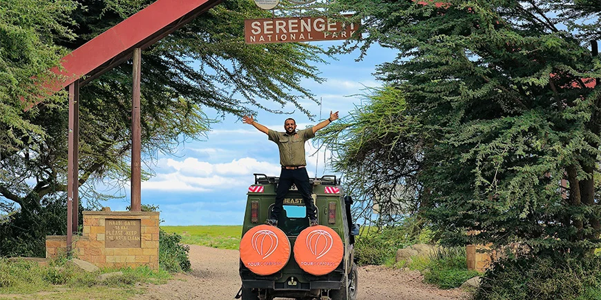 Safari-gids Madeal voor het Serengeti-bord bij de safarijeeps van TourCompass
