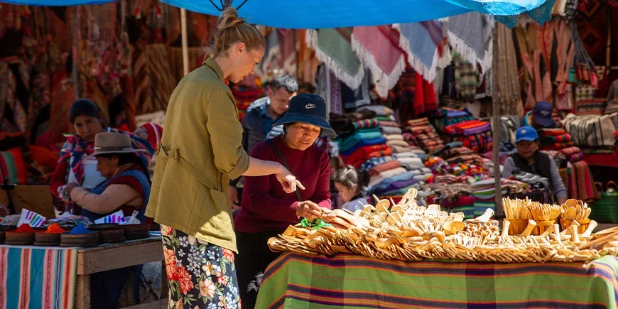 Vrouw in gesprek met een lokale verkoper over souvenirs op een markt in Cusco, Peru